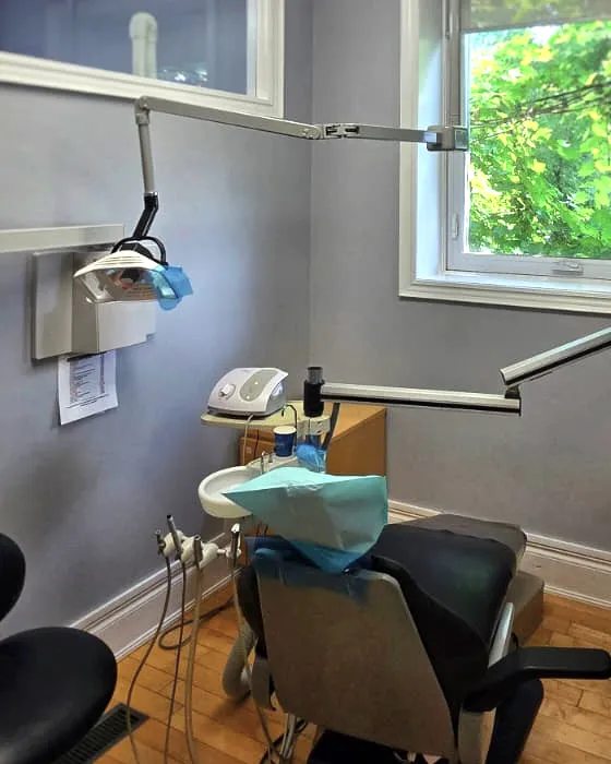 A treatment room at Clarkson Village Dental, with the chair prepared, the examination light overhead and daylight coming through a window onto the wood floor